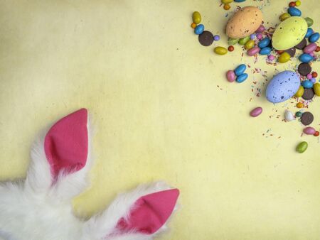 Cute creative composition with wooden easter eggs, colorful sweets, and bunny ears. Easter and...