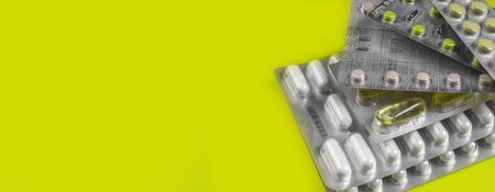 Capsules and pills packed in blisters on yellow background. Tablets. Medicine symbol. Medications drugs. Copy spaceの写真素材