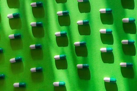 Pattern of white and green pills on a green background. Heap of medicine tablets with trendy shadow. Healthcare or medicament addiction concept. Pharmacy themeの写真素材