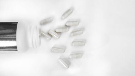 capsules or tablets spilling out of pill bottle and isolated on white. Top view. Copy space. Medicine conceptの写真素材