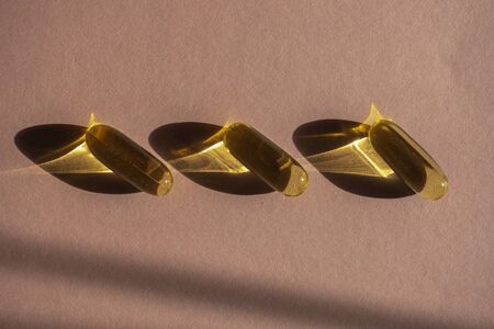 Oil yellow gelatin capsules on pink background with flower shadow, vitamins and antioxidant concept Omega 3, liver cod or evening primose oil for healthcare. Minimalism. Copy space.の写真素材