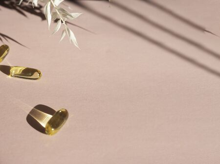 Oil yellow gelatin capsules on pink background with flower shadow, vitamins and antioxidant concept...
