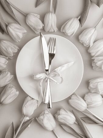 monochrome composition for Easter with tulip and white plate with fork and knife cutlery and decorative bow. Top view. Happy easter conceptの写真素材