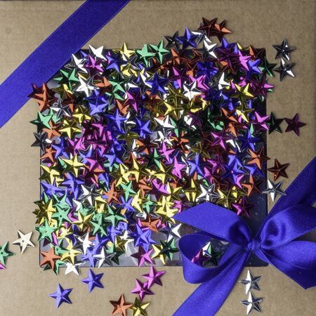 craft gift or present box with satin blue ribbon bow and colorful decorative stars on trendy blue background, Flat lay. Greeting festive card for birthday, christmas, holiday.の写真素材