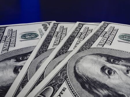 Stack of many hundred dollar bills on blue background, close-up.