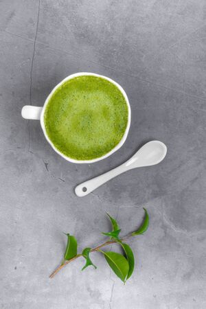 Matcha green tea latte beverage in white ceramic cup with spoon, green leaf on concrete grey background, top view, copy spaceの写真素材