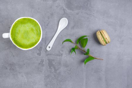 French almond cake makarons, green leaf, matcha tea in white cup with white spoon on concrete backgroundの写真素材