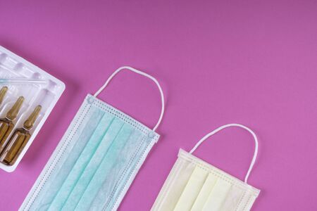disposable medical masks and ampoules on pink background, a typical 3-layer surgical mask for...