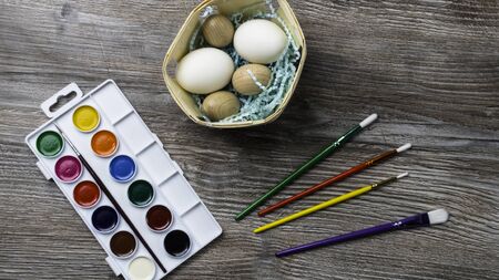 easter eggs in nest and colorful paints and brushes on wooden background. Beginning to painting. Close upの写真素材