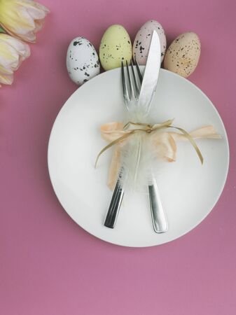 Beautiful luxury easter table cutlery settings as knife, fork with colorful tulips frame on pink...