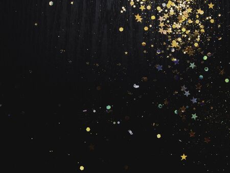 unfocused black textured wooden surface with colorful glitters, gold stars on vintage background....