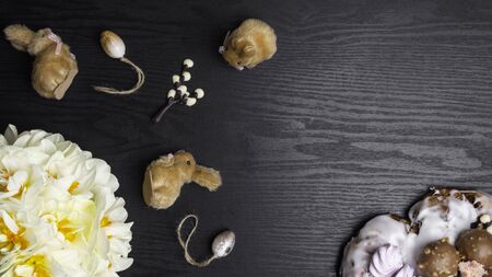 chocolate willow branches, cute bunnies with eggs, pretzel, narcissus flowers on black wooden...