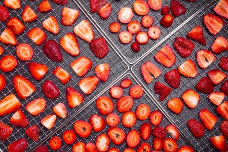 sliced ripe strawberries in dehydrator trays on wooden background, fresh berries macro. Healthy...