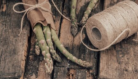 Bunch of fresh organic asparagus wrapped in craft paper, tied with twine on a old rustic wood background. Selective focusの写真素材