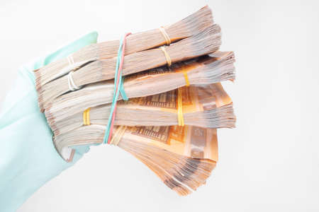 Hand projected with rubber glove holding, receiving or giving wad of European union Euro money cash banknotes, prevention virus spread, world money concept Corona virus COVID-19 outbreak.の写真素材