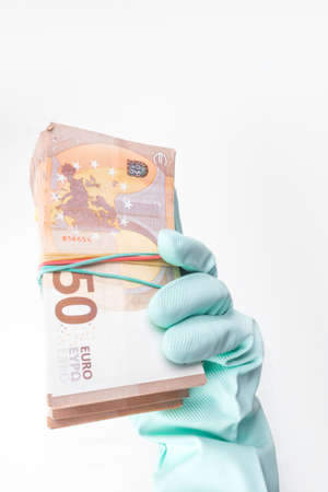 Hand projected with rubber glove holding, receiving or giving wad of European union Euro money cash banknotes, prevention virus spread, world money concept Corona virus COVID-19 outbreak.の写真素材