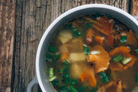 bowl of soup with autumn chanterelles and herbs, green onion on rusrtic wooden background. Vegetarian Russian cuisineの写真素材