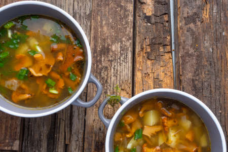 bowls of soup with autumn chanterelles and herbs, green onion on rusrtic wooden background. Vegetarian Russian cuisineの写真素材