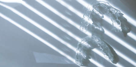 Modern tooth transparent aligners or braces to straighten teeth in cosmetic dentistry and orthodontics with trendy flower shadows, selective focusの写真素材