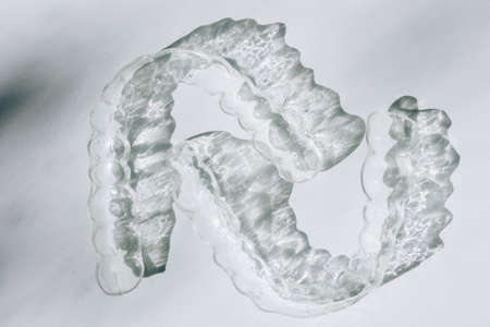 Modern tooth transparent aligners or braces to straighten teeth in cosmetic dentistry and orthodontics with trendy shadows, selective focusの写真素材