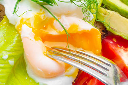 macro photo of healthy breakfast with poached spilled egg, salad, tomato and avocado, close upの写真素材