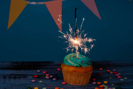 Birthday or christmas cupcake with a sparkler, against a blue background, dark toned, selective focusの写真素材