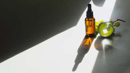 Fresh grape and grapeseed oil in glass bottle, with glass transparent sphere. Alternative medicine concept. Bio organic essential herbs oil rich in antioxidant. Healthy food. Anti aging skin care cosmetics. Selective focus. Trendy shadowsの写真素材