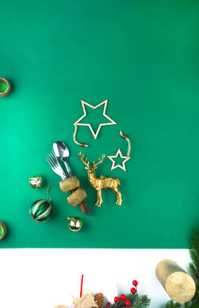 Festive table cutlery setting on green background, with festive decoration, deer toy, stars. Beautiful flat lay arrangement.の写真素材