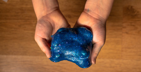 children stretching blue slime with stars glitters to the sides. Kids hands playing slime toy on...