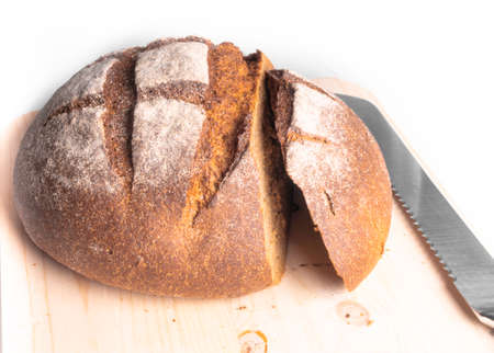 freshly baked wholemeal bread sliced on wooden board, round traditional tasty bread and cutting...