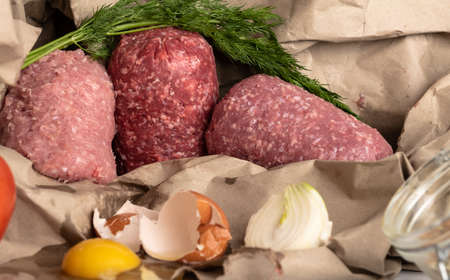 raw ingredients for cutlets, meat patties, organic mixed minced meat, egg, onion, herbs, salt, pepper, tomato, dill on paper eco backgroundの写真素材