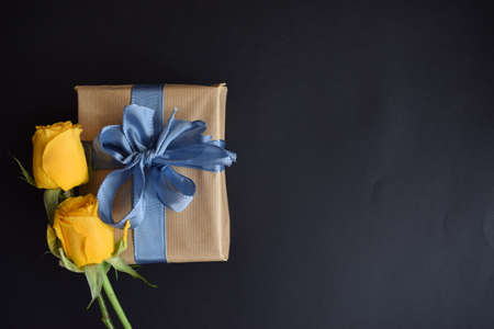A gift and two yellow roses on a black background