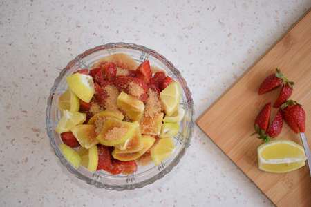 A bowl of strawberries, a lemon and brown sugar. The ingredients of a lemonade.の写真素材