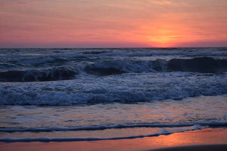 A beautiful sunset on the beach in the turbulent oceanの写真素材