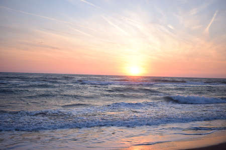 A beautiful sunset on the beach in the turbulent oceanの写真素材