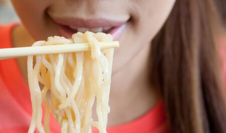 Noodle on chopsticks with woman in the background, Shallow depth of fieldの写真素材