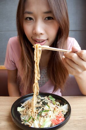 Asian young girl eating japanese noodle style with chopsticksの写真素材