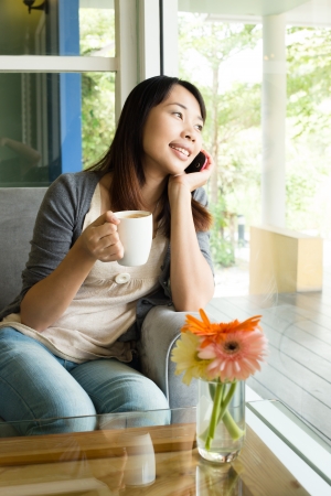 Young woman drinking  hot coffee and talking on phone in  sidewalk cafeの写真素材