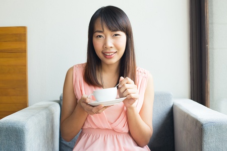 Happy woman having  morning coffee on the  sofa in bedroomの写真素材