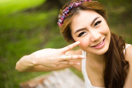 Portrait of young beautiful woman smiling and showing  the ring in the parkの写真素材