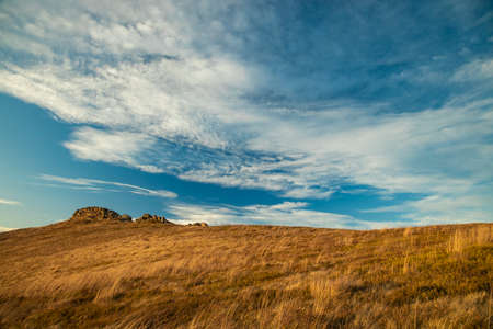 autumn time yellow grass highland meadow of mountain ridge scenic landscape nature view with rock and vivid colorful cloudy blue sky moody weatherの写真素材