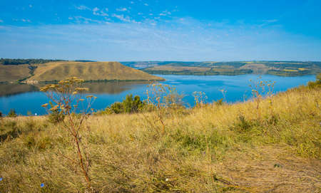 summer time grass hill land picturesque nature reservation scenic view with lake smooth calm water in clear weather dayの写真素材