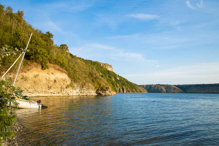 summer time peaceful lake waters on edge of forest and green hill land nature reserve environment with white yacht, copy space for textの写真素材