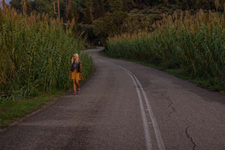 lonely young girl without home go along country side road surrounded by cereals fieldsの写真素材