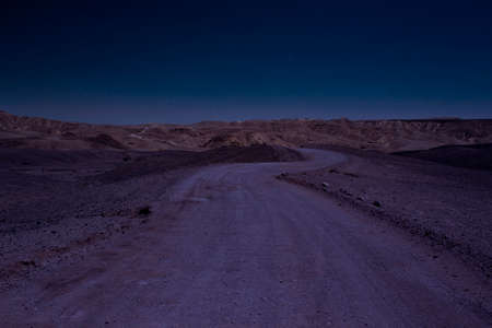 long exposure desert night scenery landscape with stars blue sky photography of wasteland country side gravel road go to mountains on horizon lineの写真素材