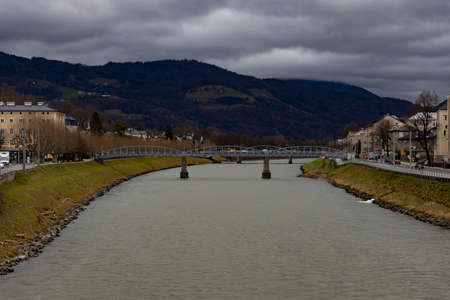 Salzburg Austria old European town outskirts landmark view with bridge across river and mountain silhouette landscape background in gray rainy dayの写真素材