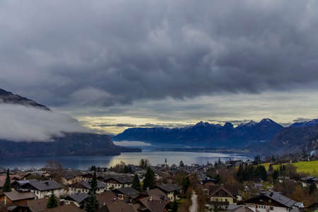 European village in Austria landmark country side scenic view settlement near lake with snowy peaks of mountain landscape background in autumn dramatic cloudy weatherの写真素材