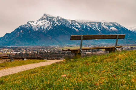 Alps mountains scenery landscape snowy range peak background with lonely wooden bench foreground beautiful view point peaceful and loneliness atmosphere in spring timeの写真素材