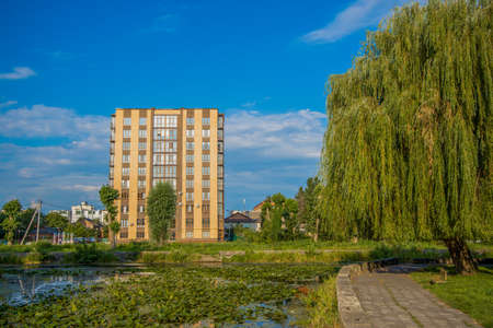 green city scene view on common living building from park outdoor natural zone with trees small lake and walking trail summer timeの写真素材