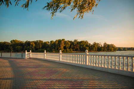 evening sunset peaceful soft colors time river waterfront white marble fence and island background European park City square walking and promenadeの写真素材